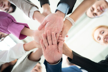 Under view of group of business people joining hands together in office to empower each other