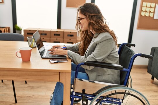 Young beautiful hispanic woman business worker using laptop sitting on wheelchair at office