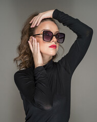 Woman with sunglasses  and black blouse against a grey background. Style beauty girl with red lips.Portrait of stunning young woman in sunglasses look into the camera