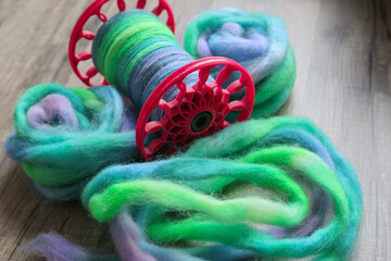 Modern spindle spool of a spinning wheel with handspun yarn on it and colourful sheep wool ready...