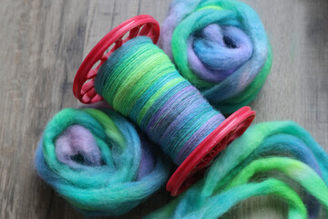 Modern spindle spool of a spinning wheel with handspun yarn on it and colourful sheep wool ready...