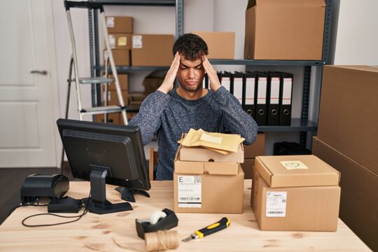 Young hispanic man working at small business ecommerce using smartphone pointing finger up with successful idea. exited and happy. number one.