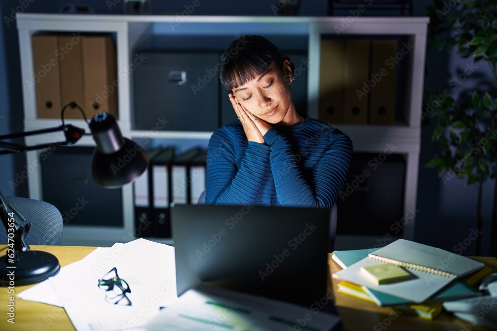 Sticker Young beautiful woman working at the office at night sleeping tired dreaming and posing with hands together while smiling with closed eyes.