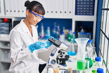 Young beautiful hispanic woman scientist smiling confident using microscope at laboratory