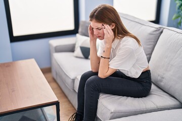 Young blonde woman stressed sitting on sofa at home