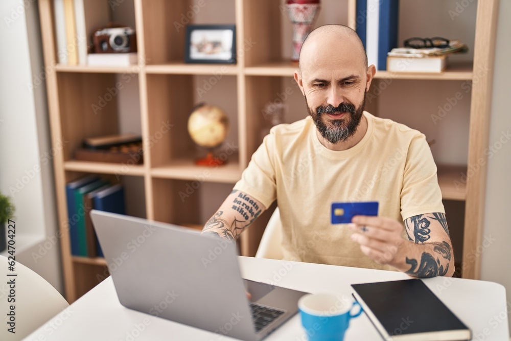 Canvas Prints Young bald man using laptop and credit card sitting on table at home