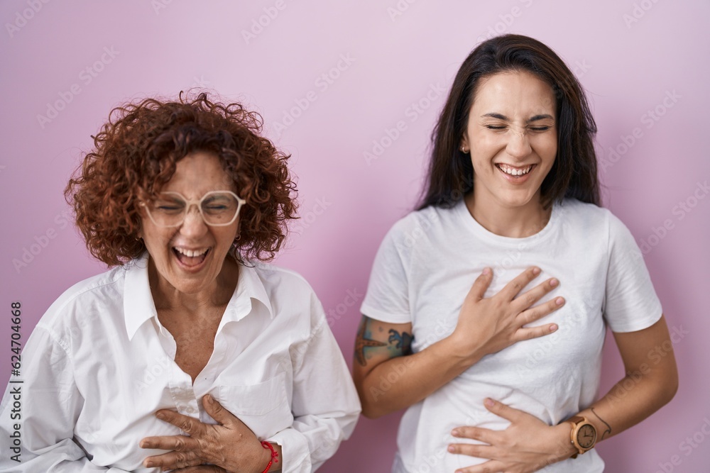 Wall mural Hispanic mother and daughter wearing casual white t shirt over pink background smiling and laughing hard out loud because funny crazy joke with hands on body.