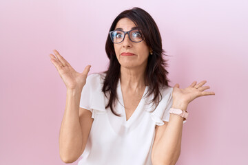 Middle age hispanic woman wearing casual white t shirt and glasses clueless and confused expression...