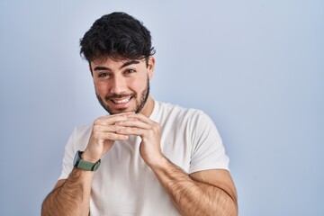 Hispanic man with beard standing over white background laughing nervous and excited with hands on...