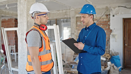 Two men builder and architect writing document speaking at construction site