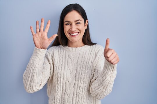Young brunette woman standing over blue background showing and pointing up with fingers number six while smiling confident and happy.