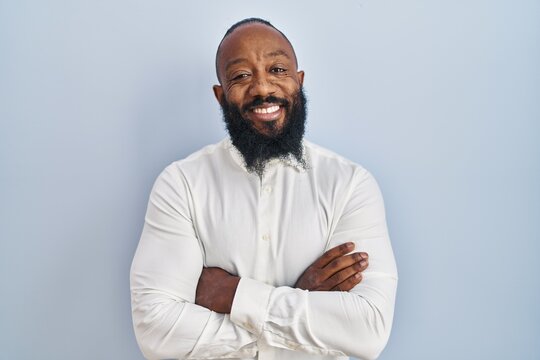 African american man standing over blue background happy face smiling with crossed arms looking at the camera. positive person.
