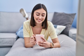 Young hispanic woman drinking coffee lying on sofa at home