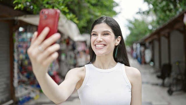 Young beautiful hispanic woman smiling confident making selfie by the smartphone at street market