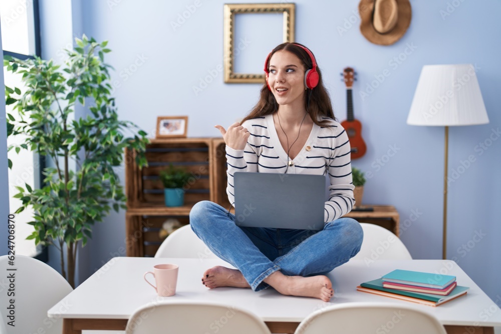 Poster Young hispanic girl using laptop at home pointing thumb up to the side smiling happy with open mouth