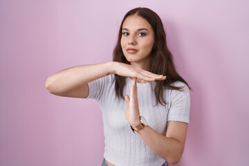Young hispanic girl standing over pink background doing time out gesture with hands, frustrated and serious face