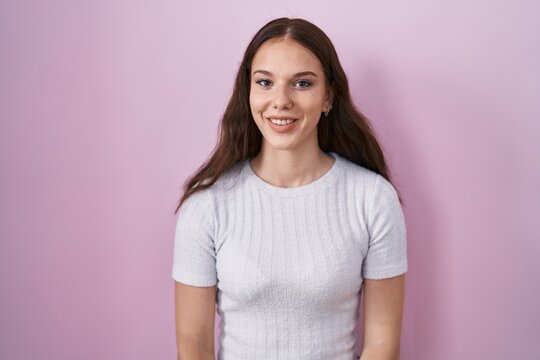 Young hispanic girl standing over pink background with a happy and cool smile on face. lucky person.