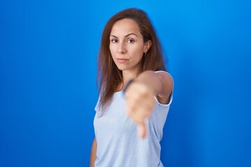 Brunette woman standing over blue background looking unhappy and angry showing rejection and...