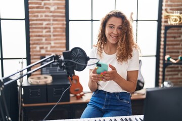 Young beautiful hispanic woman musician smiling confident using smartphone at music studio