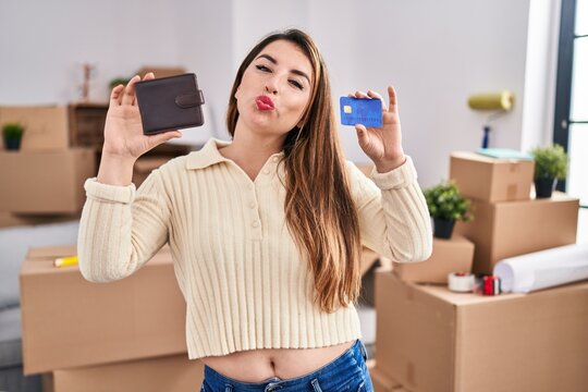 Young Hispanic Woman Moving To A New Home Holding Wallet And Credit Card Looking At The Camera Blowing A Kiss Being Lovely And Sexy. Love Expression.