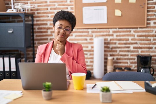 Young African American Woman Working At The Office Wearing Glasses Smiling Looking Confident At The Camera With Crossed Arms And Hand On Chin. Thinking Positive.