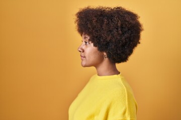Young african american woman standing over yellow background looking to side, relax profile pose with natural face with confident smile.