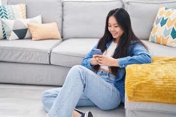Young chinese woman using smartphone sitting on floor at home