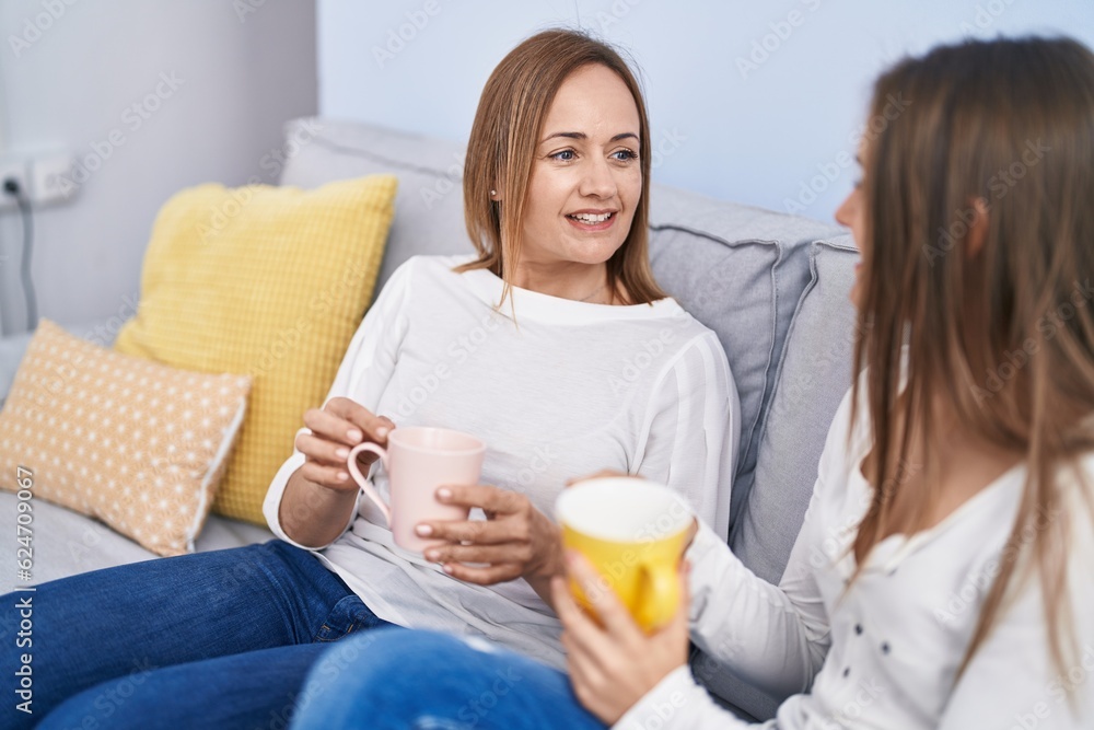 Poster two women mother and daughter drinking coffee sitting on sofa at home