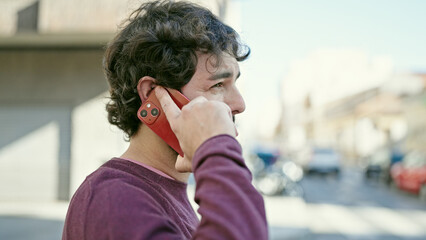 Young hispanic man talking on smartphone with serious expression at street