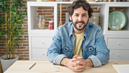 Young hispanic man smiling confident sitting on table at dinning room