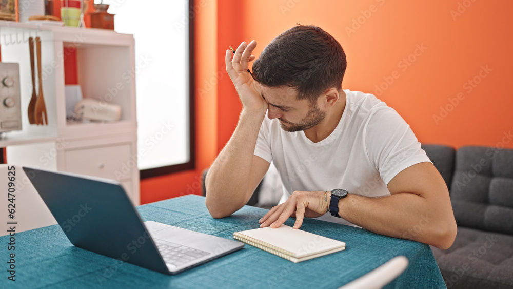 Sticker young hispanic man using laptop stressed at dinning room