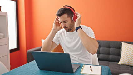 Young hispanic man listening to music sitting on table at dinning room