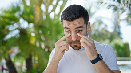 Young hispanic man standing with serious expression rubbing eyes at street