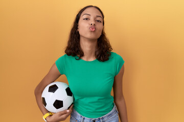 Young hispanic woman holding ball looking at the camera blowing a kiss on air being lovely and...