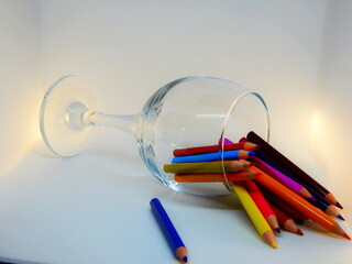 Artistic chaos: colored pencils spilled from an overturned glass, illuminated by side lighting on a gray background