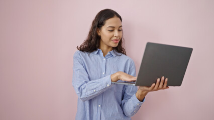 Fototapeta premium Young beautiful hispanic woman holding laptop over isolated pink background