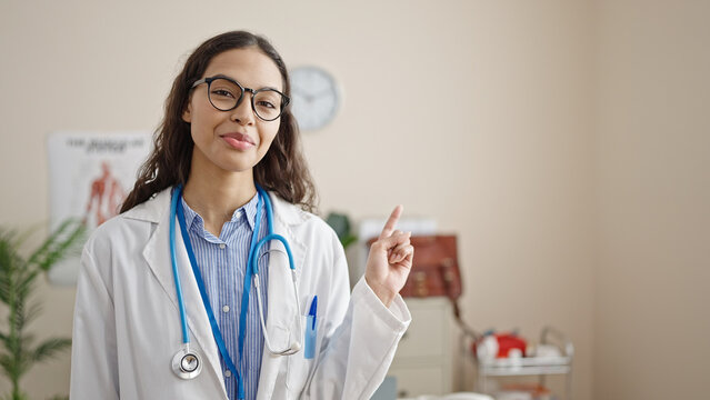 Young beautiful hispanic woman doctor smiling pointing to the side at clinic