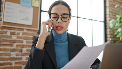 Young beautiful hispanic woman business worker speaking on the phone reading document at office