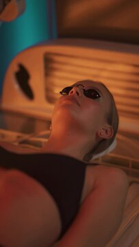 Sun treatments in a horizontal solarium, young woman takes a sun bath in a solarium, uses eye protection, warm light, vertical video for social networks.