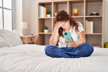 Middle age woman using smartphone wit worried expression at bedroom