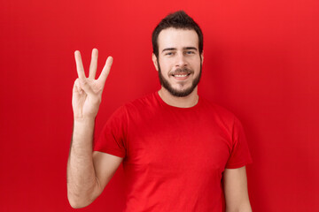 Young hispanic man wearing casual red t shirt showing and pointing up with fingers number three while smiling confident and happy.