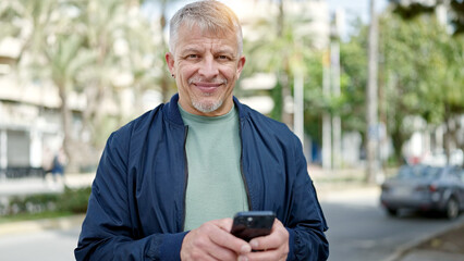 Middle age grey-haired man smiling confident using smartphone at park