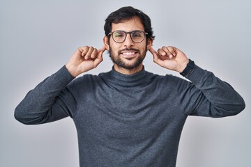 Handsome latin man standing over isolated background smiling pulling ears with fingers, funny...
