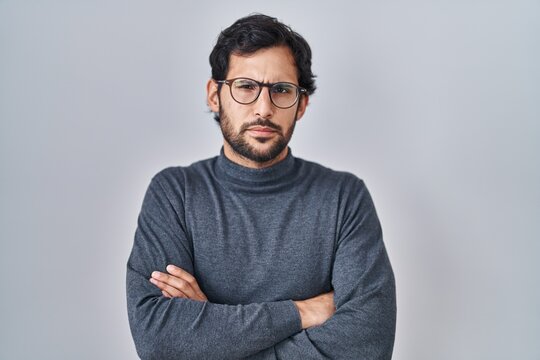 Handsome latin man standing over isolated background skeptic and nervous, disapproving expression on face with crossed arms. negative person.