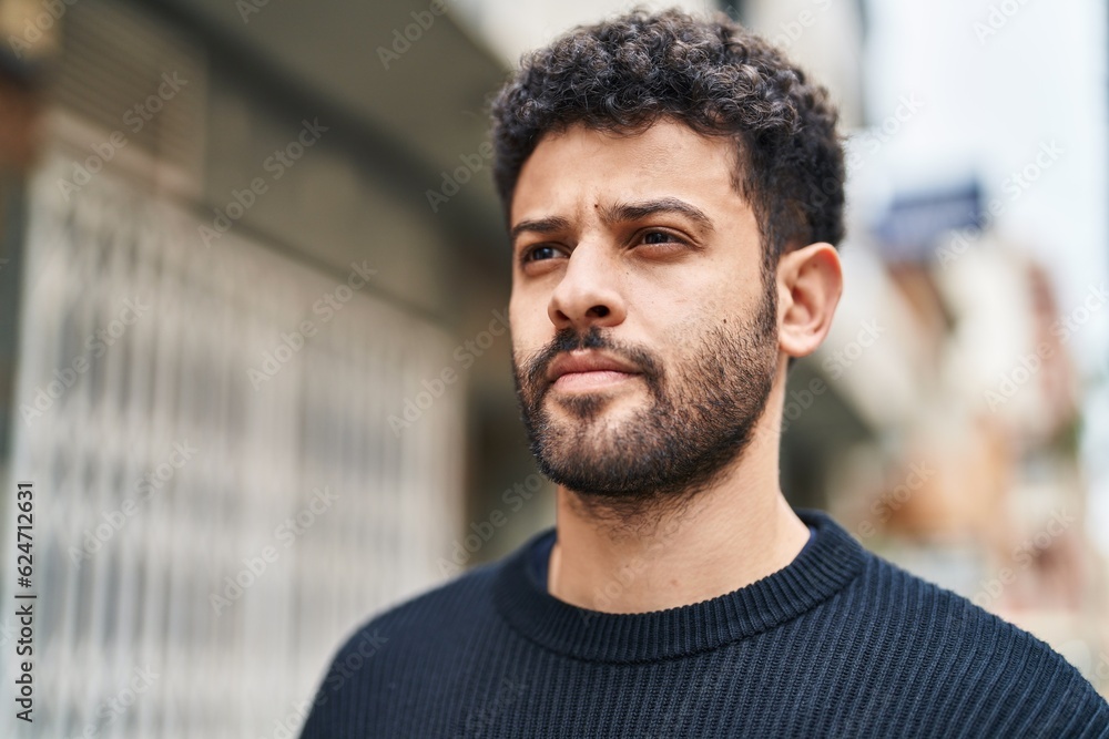 Wall mural young arab man with relaxed expression standing at street