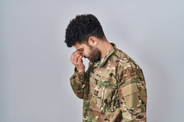 Arab man wearing camouflage army uniform tired rubbing nose and eyes feeling fatigue and headache. stress and frustration concept.