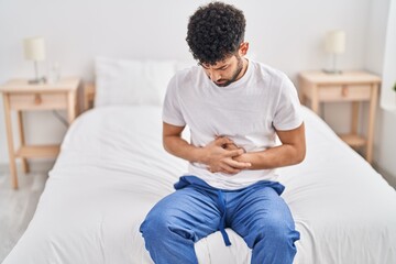 Young arab man suffering for stomachache sitting on bed at bedroom