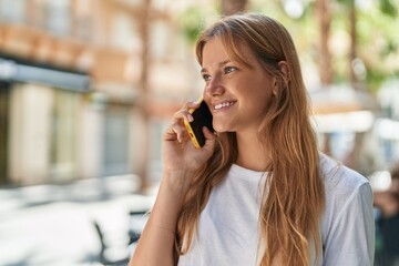 Young blonde girl smiling confident talking on the smartphone at street