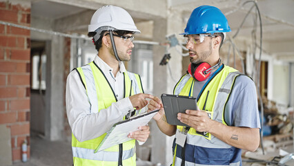 Two men builders and architect using touchpad shake hands at construction site