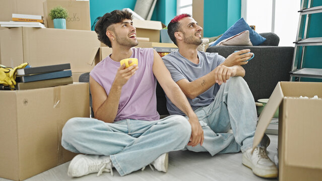 Two men couple drinking coffee sitting on floor speaking at new home - Powered by Adobe